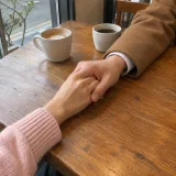 Two people holding hands across a cafe table with two cups of coffee