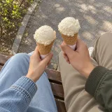 Two people on a park bench each holding an ice cream cone